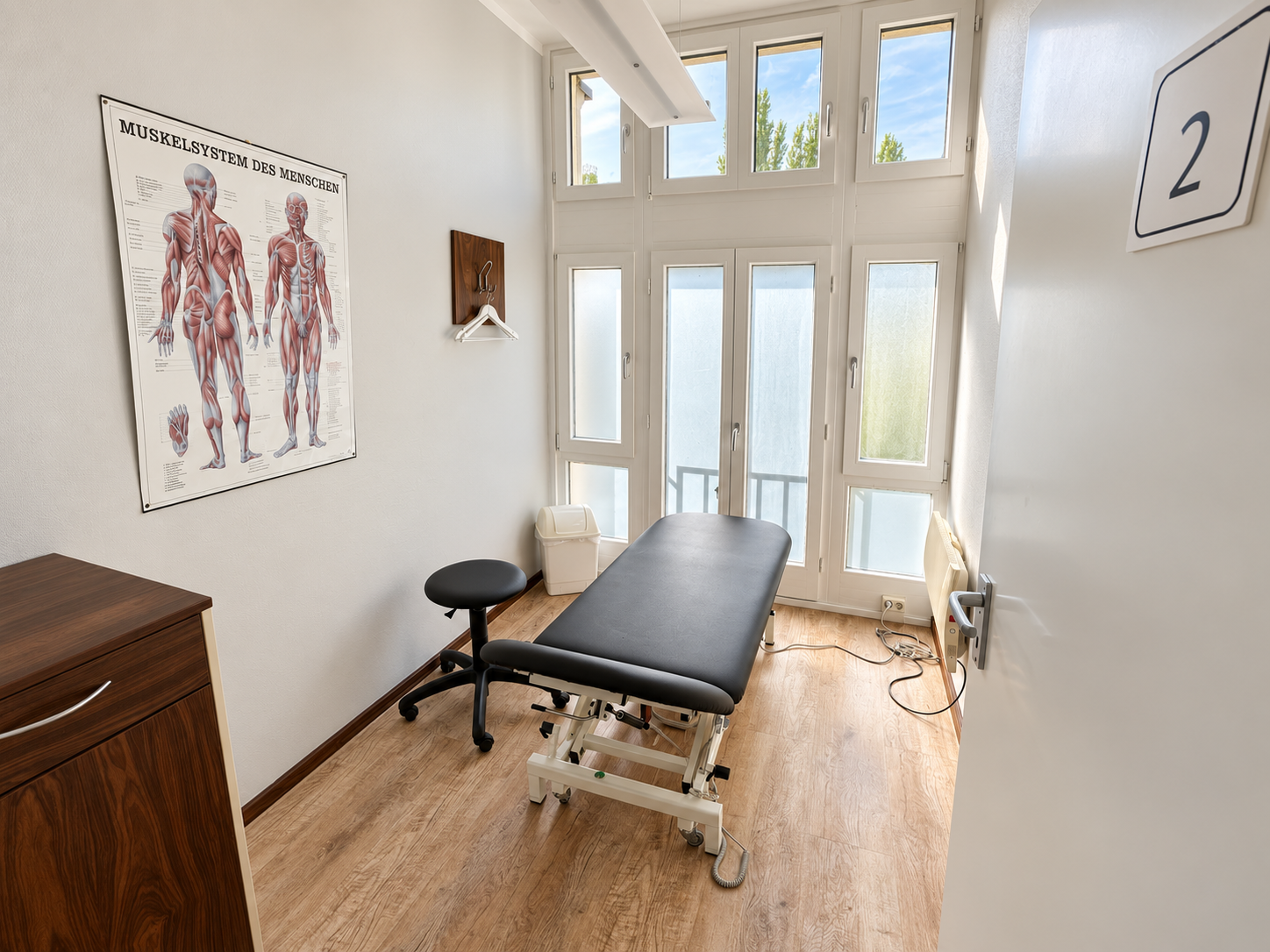 Unser Behandlungsraum mit Behandlungsliege, Stuhl und Anatomieposter